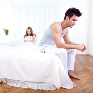 man sitting on edge of bed looking unhappy